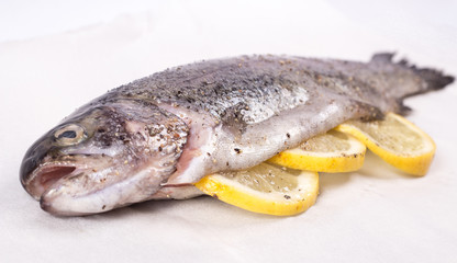 Three raw trouts on paper with thyme and lemon on a rustic wooden table