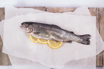 Three raw trouts on paper with thyme and lemon on a rustic wooden table