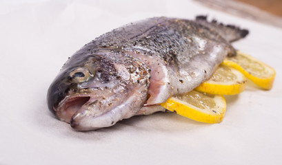 Three raw trouts on paper with thyme and lemon on a rustic wooden table