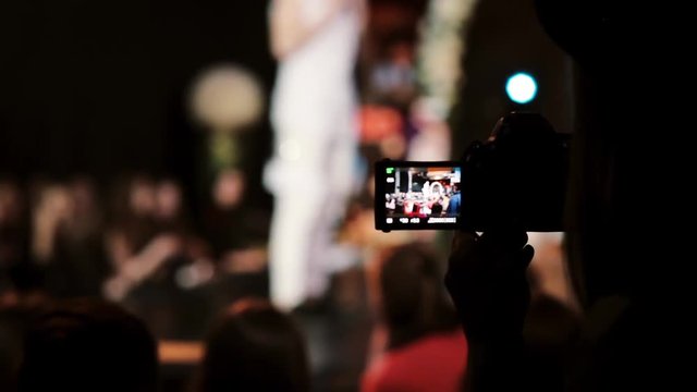 Closeup view of a girl holding camera and filming a dance. Blurred dancer on the background