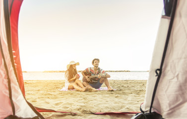 Couple of hipsters in camping playing guitar at the beach, view from inside the tent.