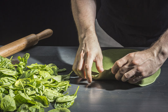 Midsection of man kneading green dough by basils at table