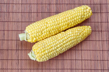 Two fresh raw corn on the cob on a bamboo napkin