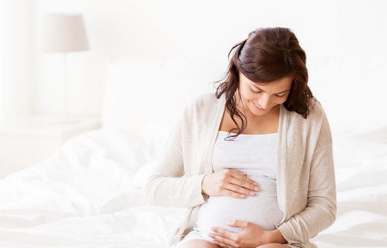 happy pregnant woman sitting on bed at home