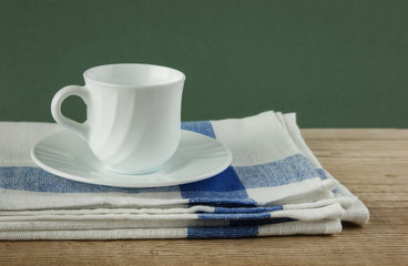 White coffee cup and dishcloth on old wooden table over green ba