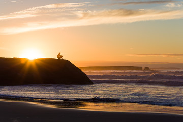 Fototapeta na wymiar a man is sitting on the rock enjoying breathtaking ocean view at sunset 