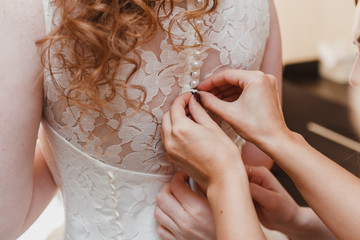 Morning bride. Bridesmaid helping the bride lacing up her dress