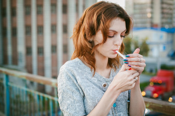 girl with a cigarette. young beautiful girl smokes a cigarette on the street. ignites the lighter,...