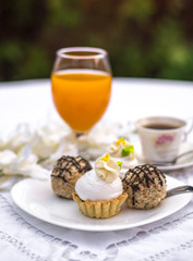 Assorted Fancy Gourmet Cupcakes on a plate. Colorful cupcakes with beautiful decoration over white vintage lace background. Surrounded by flowers, cup of coffee and glass of orange juice.