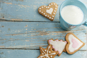 Gingerbread winter cookies with handmade icing on a blue table with a cup of milk. Heartshaped,...