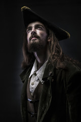 Portrait of a medieval bearded pirate thoughtfully looking up on a black background.