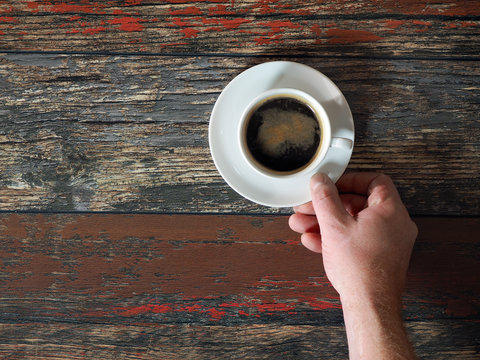 Men's large hand gently takes a small cup with a coffee drink. Wooden old boards