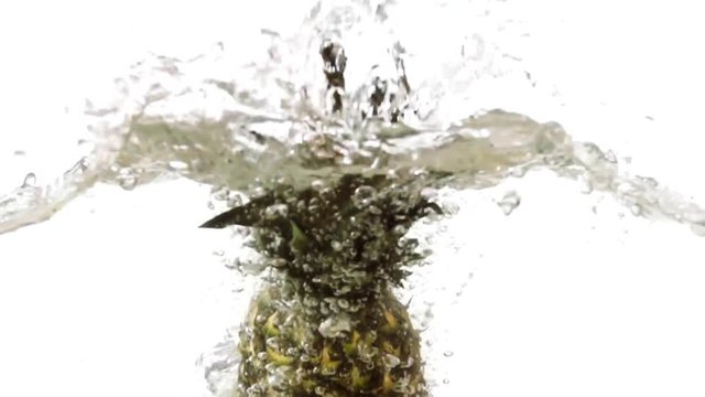 Whole pineapple falling into water on white background slow motion HD video. Water surface with floating fruits, splash bubbles and waves.