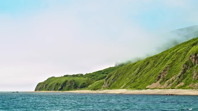 Fog moves in from the ocean over rocky seashore hills panorama