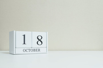 Closeup white wooden calendar with black 18 october word on blurred white wood desk and cream color...