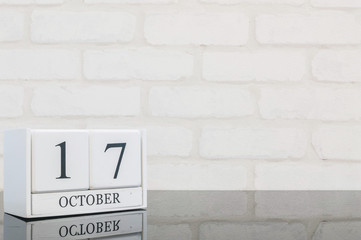 Closeup white wooden calendar with black 17 october word on black glass table and white brick wall...