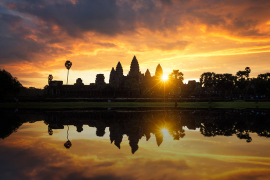 Towers of ancient temple complex Angkor Wat at sunrise. Siem Reap, Cambodia. Temple Mountain and the sun reflected in lake at dawn. Mysterious Angkor Wat is a popular tourist attraction.