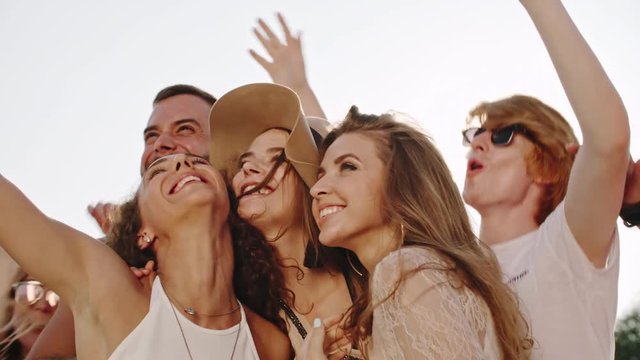Joyous young woman taking picture with her smart phone with friends while partying outdoor at summer day