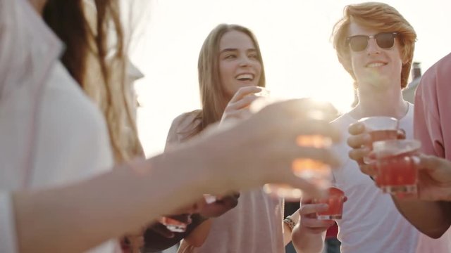 Group of friends dancing together outdoor at sunny summer day with cocktails, toasting and drinking