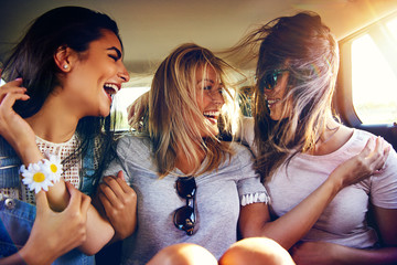 Three vivacious young women in the back of a car - obrazy, fototapety, plakaty