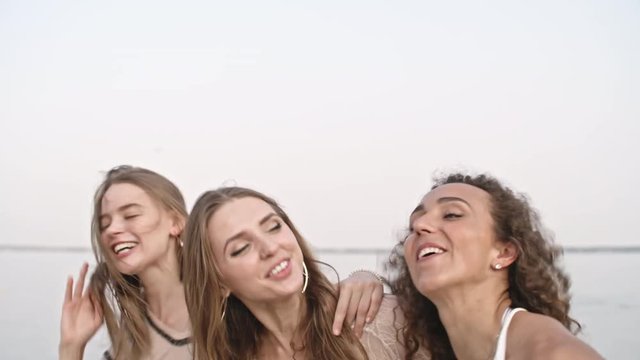 Slow motion shot of three pretty young women laughing while embracing and dancing on the beach
