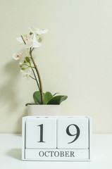 Closeup white wooden calendar with black 19 october word with white orchid flower on white wood desk and cream color wallpaper in room textured background , view another more date in my portfolio