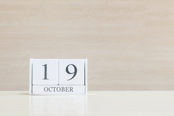 Closeup surface white wooden calendar with black 19 october word on blurred brown wood desk and wood wall textured background with copy space , view another more date in my portfolio