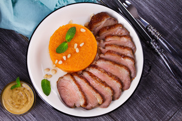 Roast duck breast and pumpkin mash, served with mint and pine nuts. Slices of duck with sweet butter squash, mustard and honey sauce. View From Above, Top Studio Shot