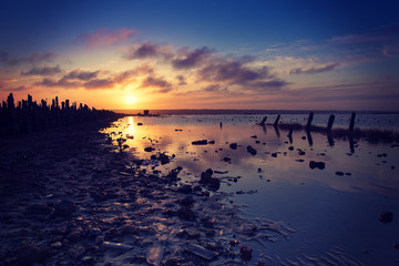 Beautiful sunny red colorful sunset on the lake with stones, wooden posts and reflection, natural seasonal summer vacation background