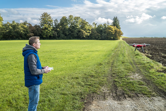 Junger Mann steuert seine Drohne zwischen Acker und grüner Wiese