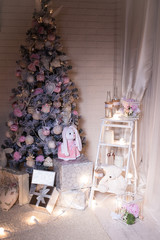 Pink Christmas tree and gift boxes under it at the white brick wall background in a white children room.