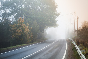 Empty rural road in autumn foggy morning
