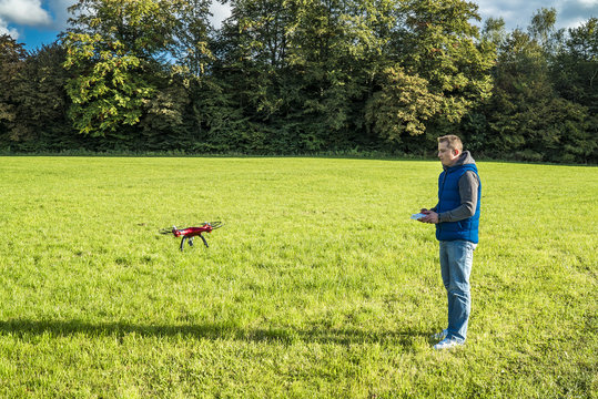 Mann fliegt seinen Quadrocopter über eine grüne Wiese