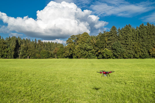 Roter Quadrocopter über grüner Wiese unter weiß-blauem Himmel