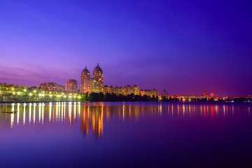 Obraz premium Embankment of modern european city with night illumination and colorful sky. Evening at the Dnieper river in Obolon, Kiev