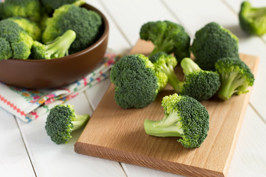 Broccoli on cutting board and in the bowl on a wooden table.
