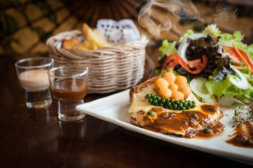 Grilled chicken steak with lettuce salad cherry tomatoes mushrooms herbs  on  white plate and wooden background. Traditional cuisine. Grill kitchen.