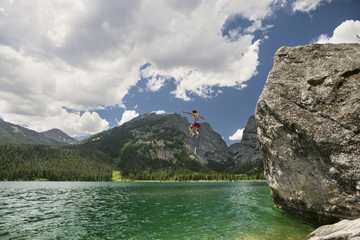 Teenager boy cliff jumping in lake against cloudy sky