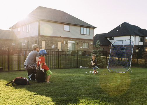 Family playing baseball at backyard on sunny day