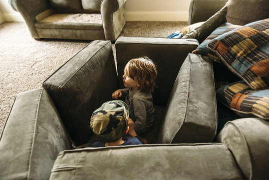 Playful boys hiding behind cushions at home