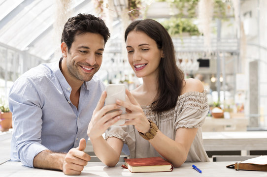 Happy Couple Using Smart Phone At Sidewalk Cafe