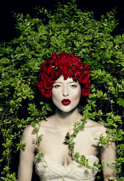 Young woman wearing red flowered headdress pouting in front of ivy plants