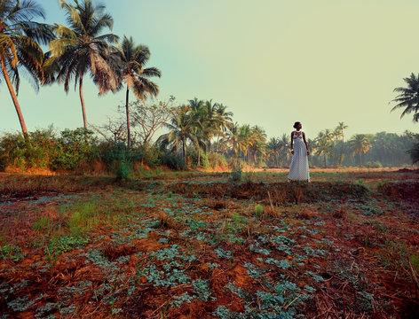 Woman wearing white dress standing in field by palm trees