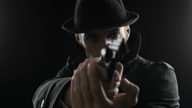 Portrait of a gangster in a hat and a black cloak takes aim with a revolver