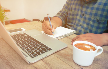 Man write on notebook with laptop and coffee cup vintage tone.