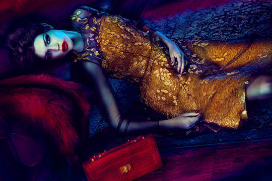 Woman in gold dress lying down with red handbag 