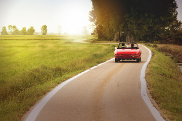 Klassisches rotes Cabrio-Auto, das bei Sonnenuntergang auf dem Land unterwegs ist
