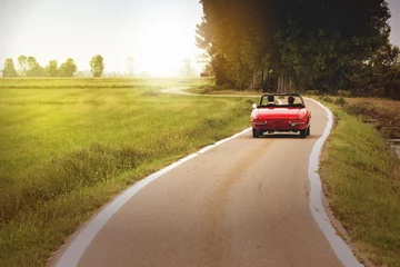 Poster Im Rahmen Klassisches rotes Cabrio-Auto, das bei Sonnenuntergang auf dem Land unterwegs ist © Arcansél