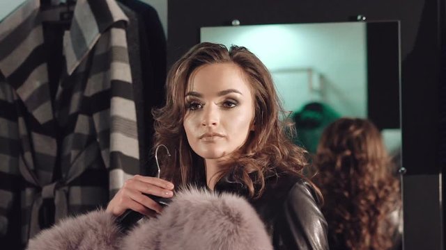Smart girl trying on the rich fur coat to the camera in boutique