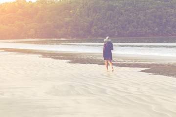 woman walking on sand beach in sunset lighting.